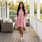 Model wearing the SWEET MOOD DRESS - Gigio in soft pink, showcasing its relaxed fit and charming style on a porch.