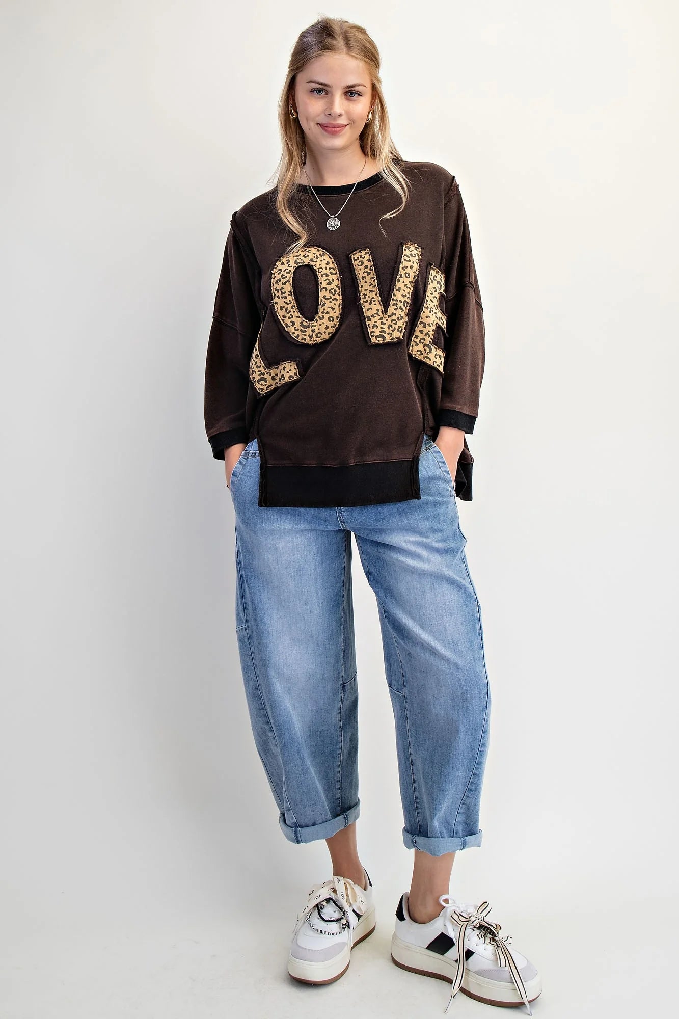 LOVE UNTAMED TOP - Easel worn by a model, featuring leopard patch letters on a dark wash terry fabric.