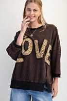 LOVE UNTAMED TOP - Easel model wearing dark wash oversized top with leopard patch letters, smiling and posing.