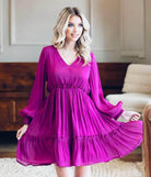 Woman wearing Bermuda Beauty Dress in jewel tone magenta with crinkle fabric, v-neckline, and balloon sleeves, standing in a room.