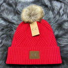 Red C.C. Warm Angle Beanie with faux fur pom pom, showcasing a distinctive diagonal pattern, perfect for warmth and style.