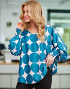 Woman wearing Blue Abyss blouse with ocean blue octagon dots and V-neck, standing indoors, showcasing elegant oversized fit by Jodifl.