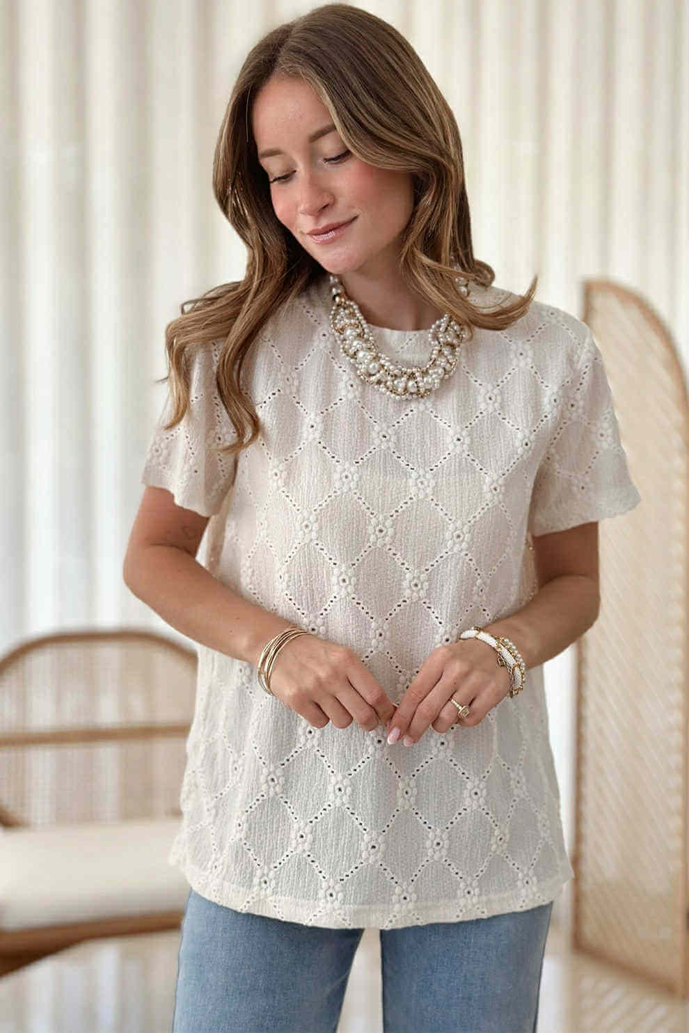 Woman wearing Lace Grace Top with geometric eyelet design and pearl necklace, styled with casual look in soft ivory.