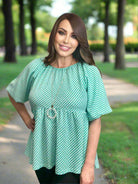 Woman wearing the Aqua Angles Top by Umgee, showcasing turquoise checkered pattern and puff sleeves in a park setting.