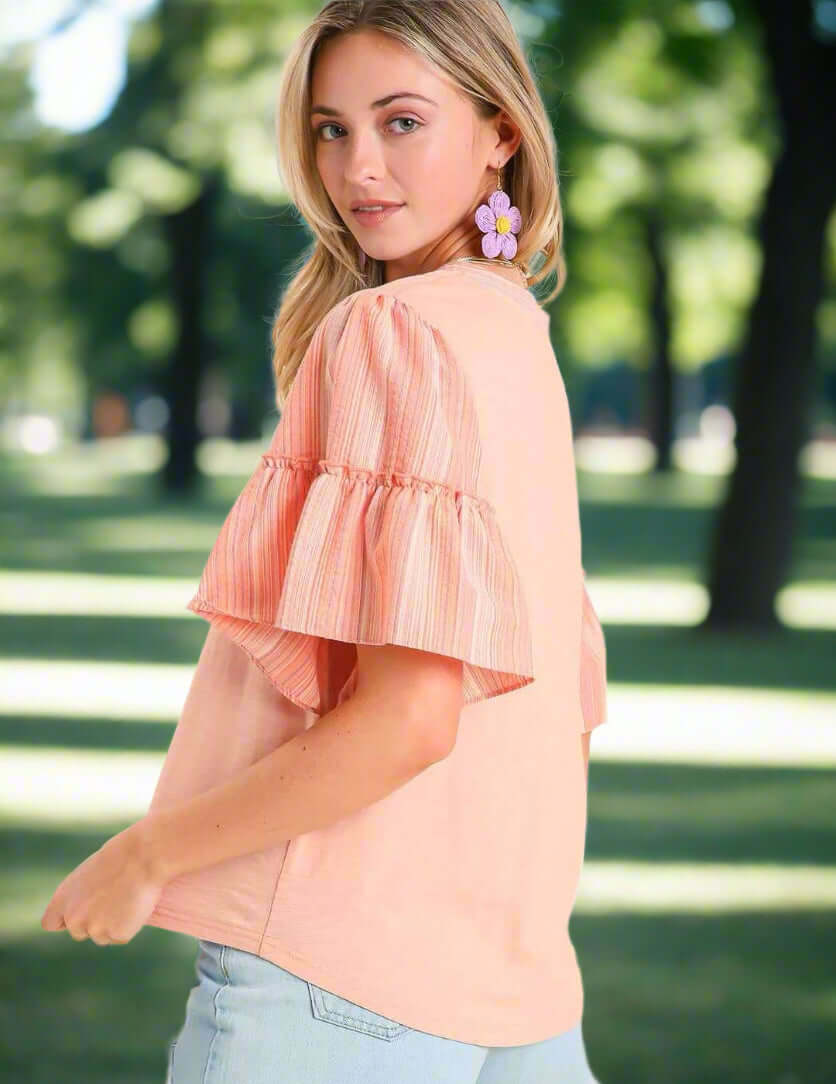 Model wearing a soft peach Ruffled Breeze cotton top with ruffle sleeves and a stylish look in a sunny park.