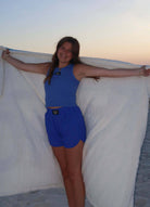 Woman joyfully showcasing LM-BK LULU MAC BLANKET PINK on the beach during sunset.