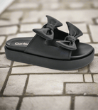 Corkys Lil Knotty black slide sandals with stylish bows, perfect for trendy casual wear.