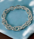 Elegant UPLINK Bracelet by Nine Jewelry in sleek silver with textured interlocking chain links, displayed on a soft blue fabric.