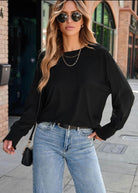 Stylish woman in a black JET SET TOP with dolman sleeves and sunglasses, paired with light blue jeans, outdoors.