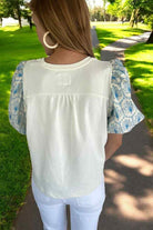Back view of woman wearing the Skylark Sweetness Top with floral puff sleeves in a sunny park.