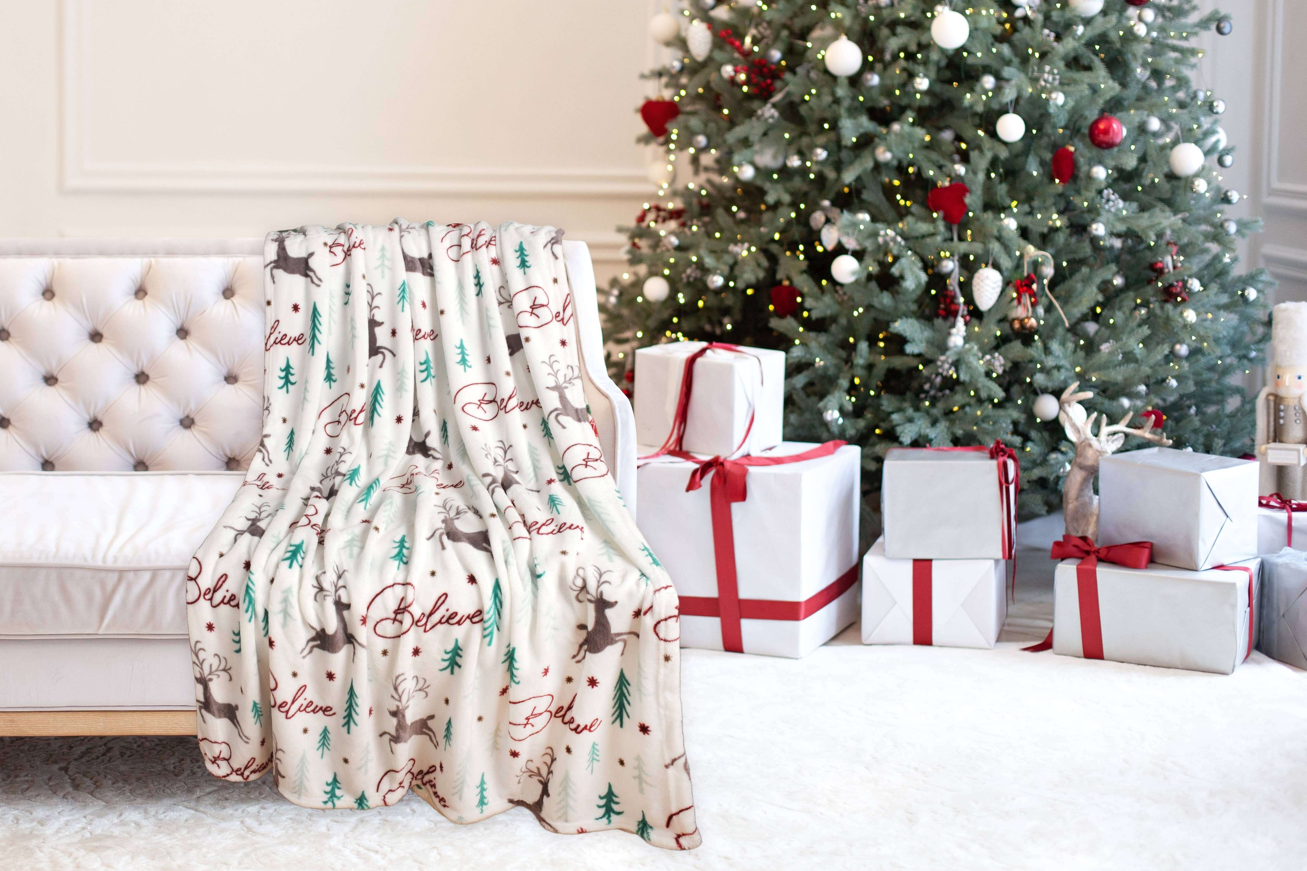 Christmas Cheer Plush Throw Blanket draped on a sofa beside a decorated Christmas tree and wrapped gifts.