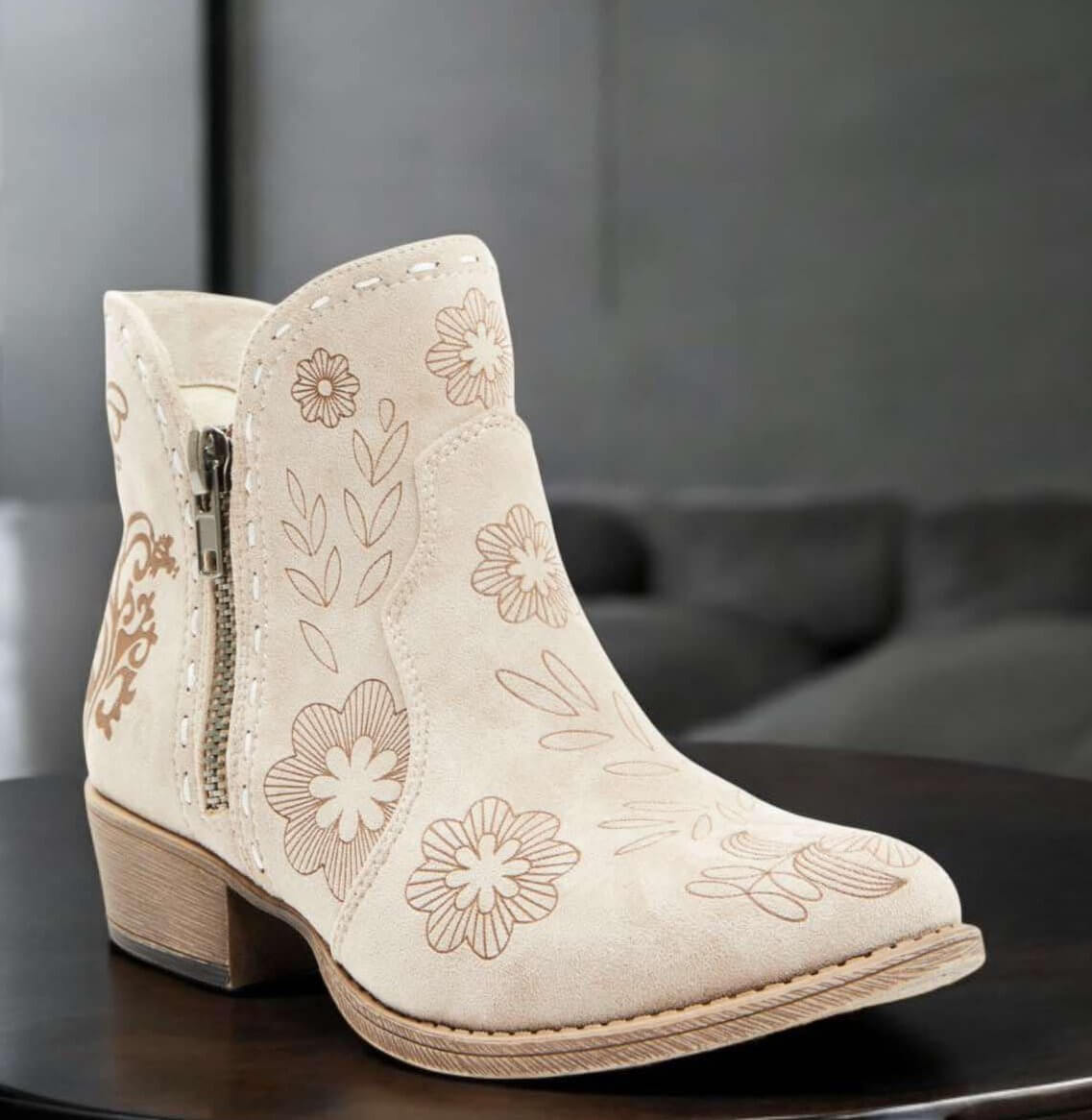 Light gray Very G Drift Bootie with floral print, faux suede upper, 1.5" heel, and zipper detail on a sleek wooden table.