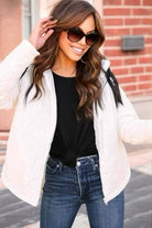 Woman wearing a chic white Wonderland puffer jacket by Umgee, paired with black top and jeans, smiling outdoors.