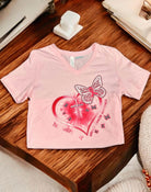 Pink FAITH HOPE LOVE T-Shirt for Breast Cancer Awareness with heart and butterfly design on a wooden table.