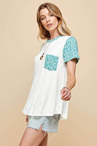 White women's short sleeve t-shirt with teal leopard print sleeves and pocket, styled with denim shorts.