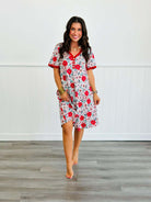 Woman wearing floral print nightgown with red accents from Shirley & Stone, standing on wooden floor.