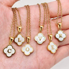 Close-up of MONOGRAM MOMENTS NECKLACE pendants, featuring gold frames and white enamel letters spelling 'CLOVER'.