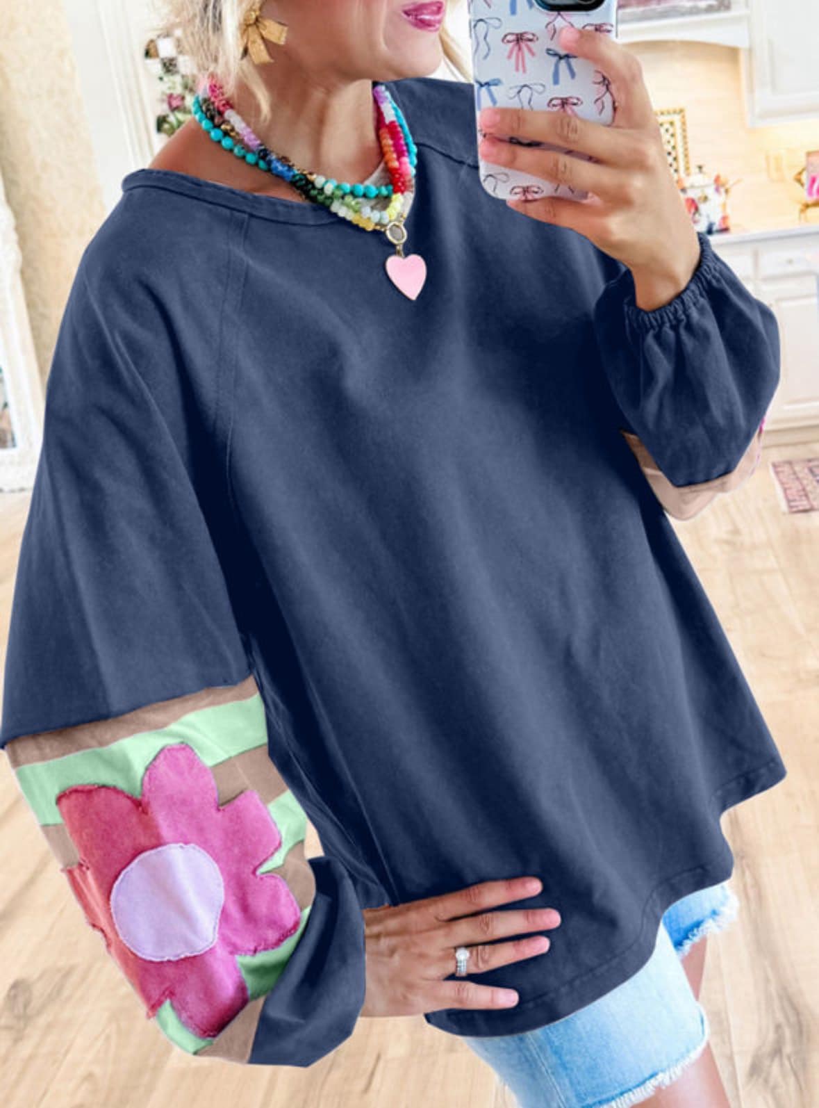 Woman wearing oversized blue pullover with vintage flair, bubble sleeves, flower applique, and raw cut details. Casual and stylish top.