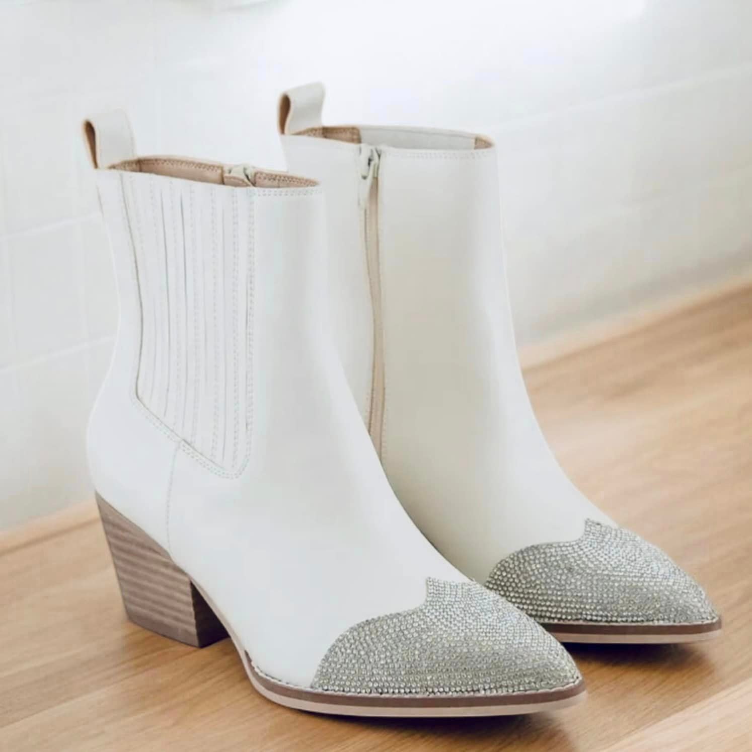 White ankle booties with rhinestone toe cap, perfect for adding elegance and glamour to any outfit. Versatile and chic footwear.