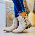 Cream faux suede Evie Bootie with distressed look and 1.5" heel, featuring zip detail and rubber sole, worn with blue jeans.