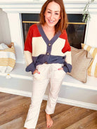 Woman wearing beige velvet joggers and a cozy multicolored sweater stands smiling in a stylish living room.