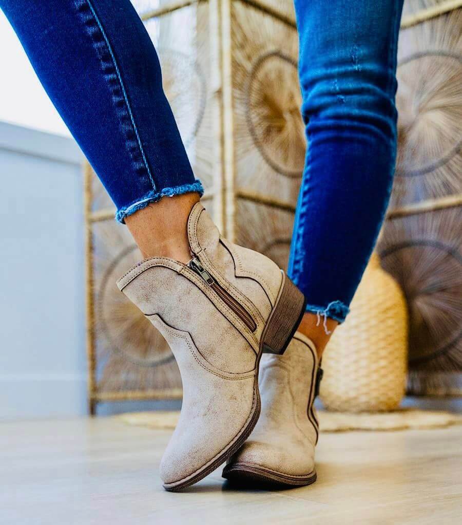 Cream Very G Evie Bootie with faux suede upper and 1.5" heel worn indoors, showcasing ankle zipper and distressed vegan leather.