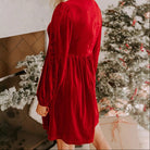 A woman in a red velvet dress poses in front of a Christmas tree, showcasing the SPARKLE SEASON VELVET DRESS (Holiday Red).