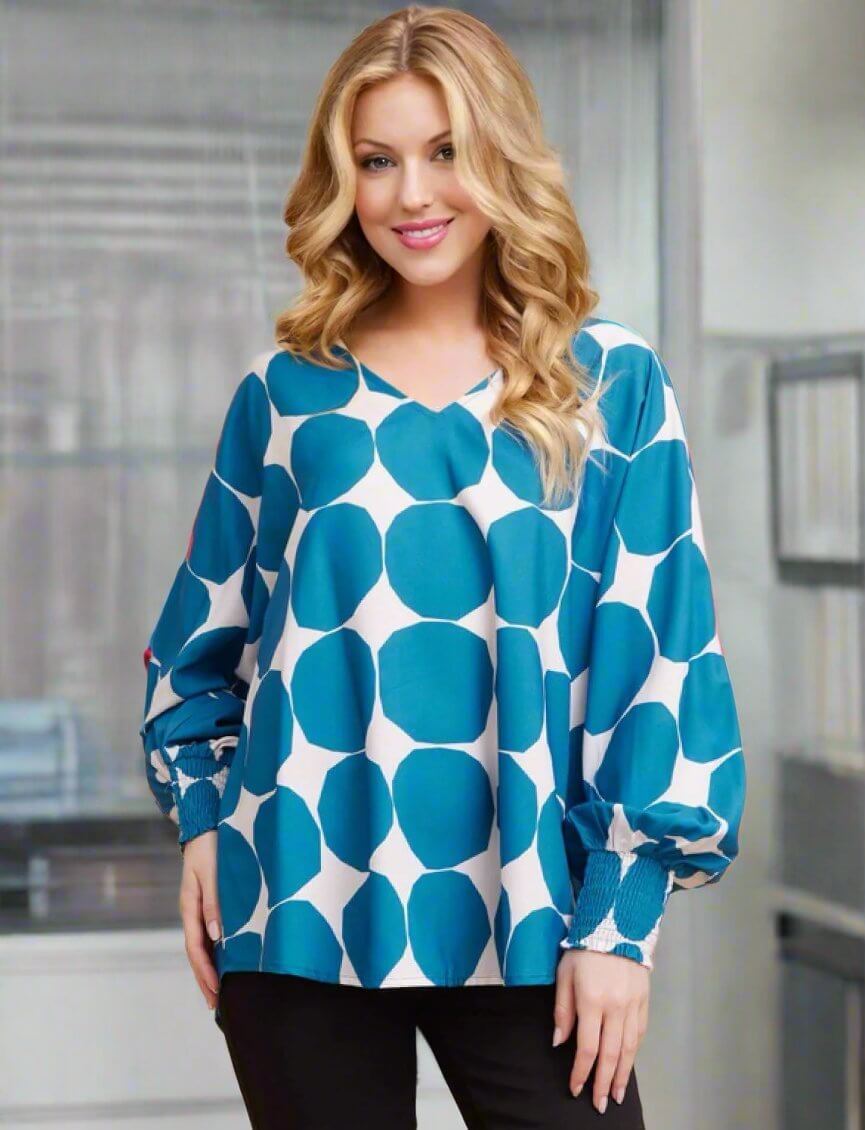 Woman wearing Jodifl Blue Abyss blouse with ocean blue octagon dots, V-neck, and smocked cuffs, showcasing oversized fit elegance.