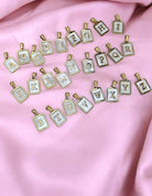 Gold letter charms A-Z on pink fabric for MP Monogram Necklace preorder, stylish and personalized jewelry option.