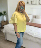 Woman wearing Ruffled Breeze lemon cotton top with ruffle sleeves and jeans in a stylish setting.