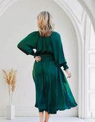 Woman wearing dark green midi dress with smocked waist and sleeves, standing in elegant archway, embodying timeless fashion and style.