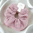 Pink pom-pom textured scrunchie on satin background, perfect for stylish hair ties and cozy accessories.