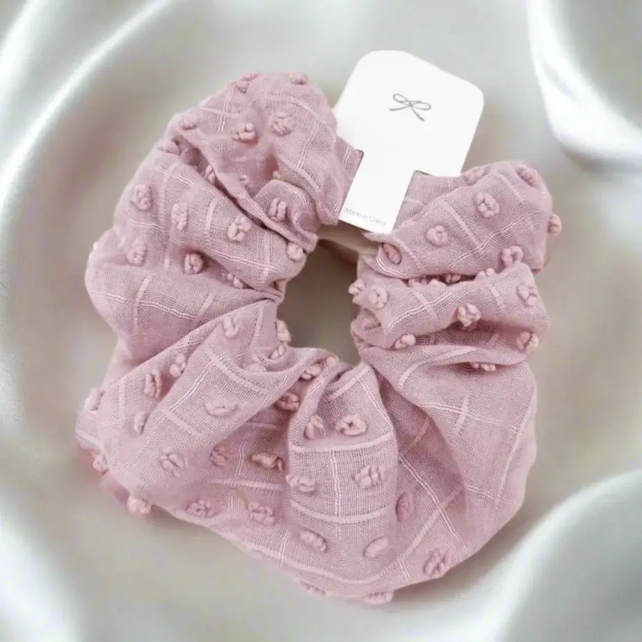 Soft pink pom-pom textured scrunchie for stylish hair or wrist wear. Ideal for adding comfort and chic flair.