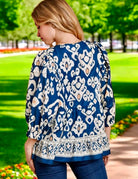 Back view of a woman wearing a blue boho chic blouse with white patterns, set in a vibrant outdoor garden.