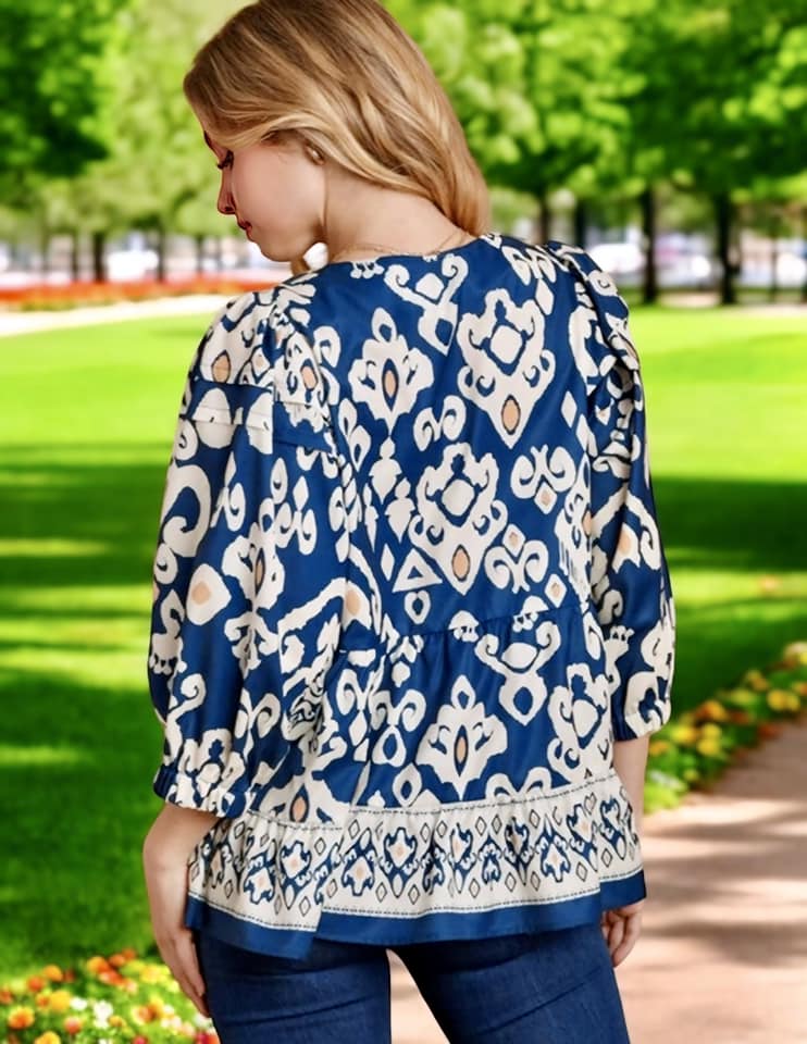 Back view of a woman wearing a blue boho chic blouse with white patterns, set in a vibrant outdoor garden.