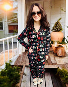 Woman wearing PEACE LOVE HOPE PJS by Love To Sleep with festive Christmas design and red trim, standing on a porch.