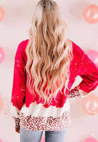 Woman with long blonde hair wearing a red Wild Hearts Crewneck with leopard print details against a pink backdrop.