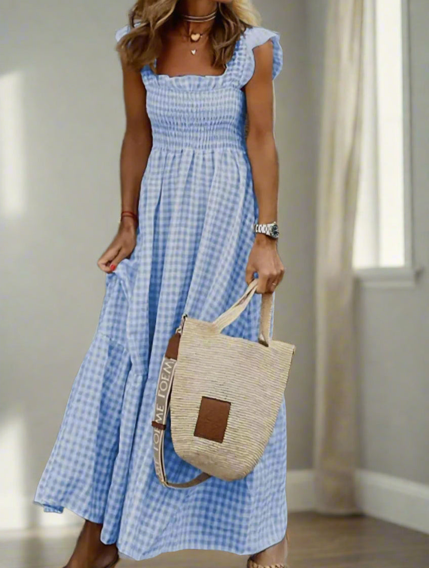 Blue gingham smocked sundress with flutter sleeves, styled with a straw bag for a charming summer look.