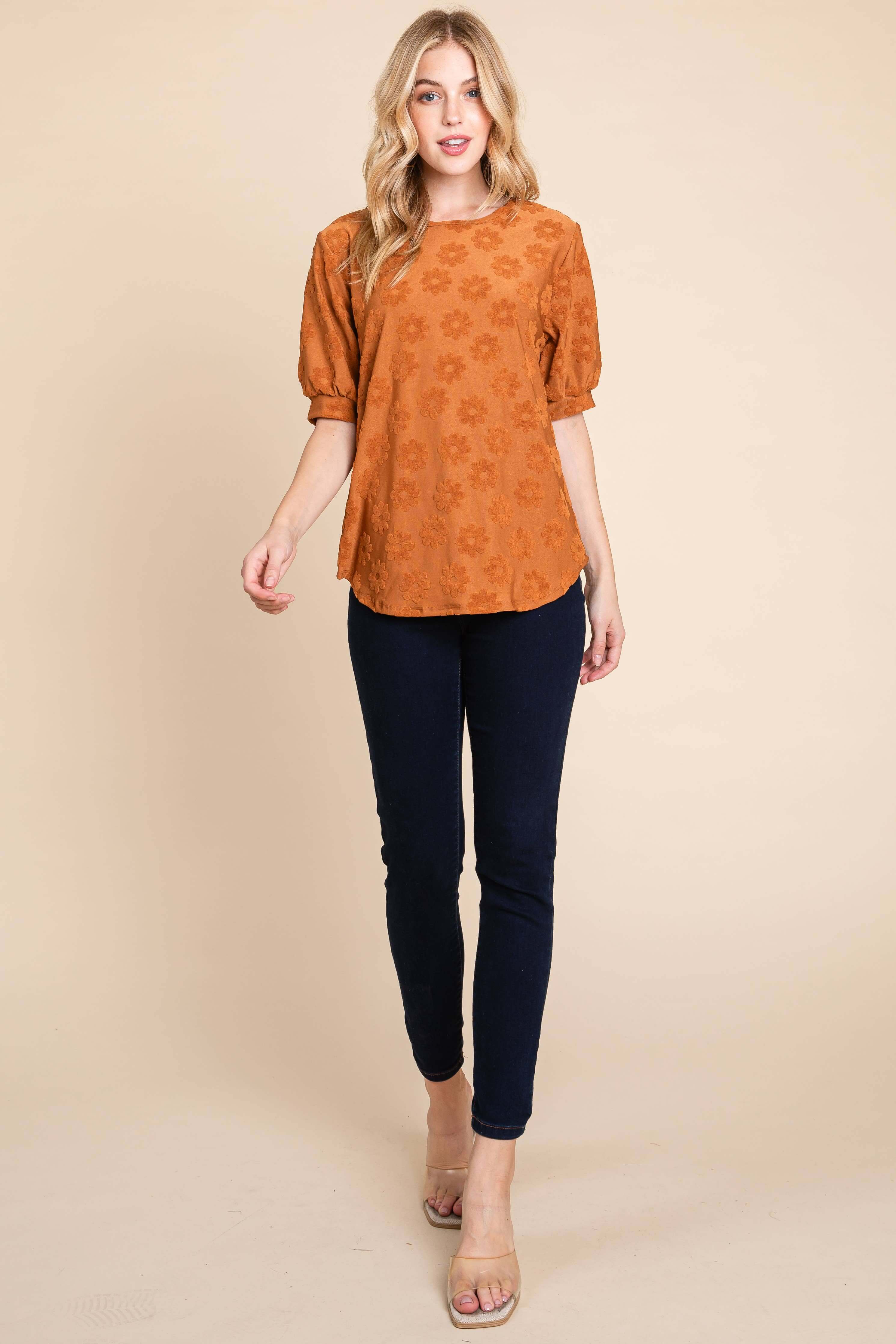 Stylish copper Field of Daisies Top with puff sleeves and textured daisy embroidery, paired with dark jeans.
