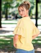 Model wearing Ruffled Breeze lemon cotton top with ruffle sleeves in a sunny park setting.