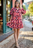 Model wearing the HAPPY MOMENTS Dress by THML, featuring a tiered ruffle skirt in geometric pink and burgundy print.