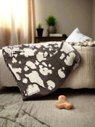 Brown Cow Blanket by Howdy Honey draped over bed, featuring playful cow pattern, adding cozy charm to home decor.