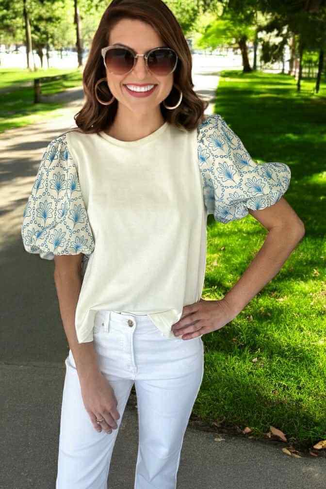 Woman wearing the Skylark Sweetness Top with sky-blue floral puff sleeves on a sunny day in a park.