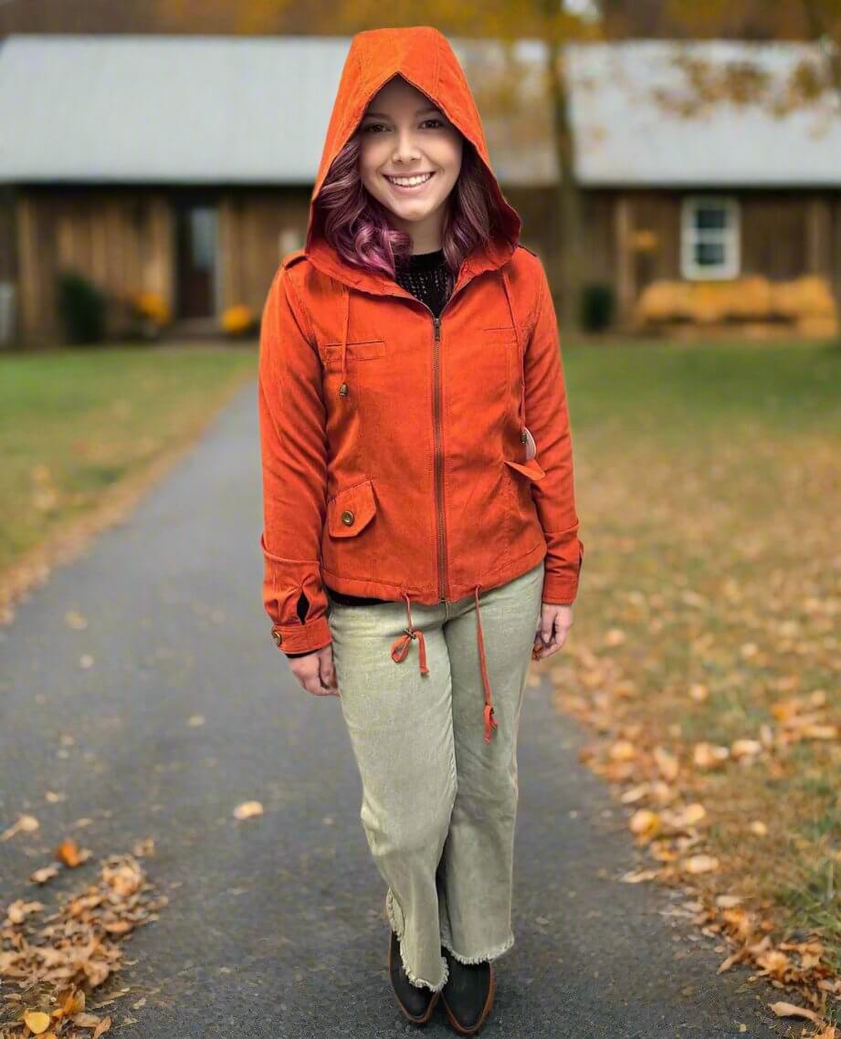 Woman wearing ginger Autumn Sunrise Jacket in a fall setting with leaves on the ground, showcasing the jacket's microfiber suede texture.