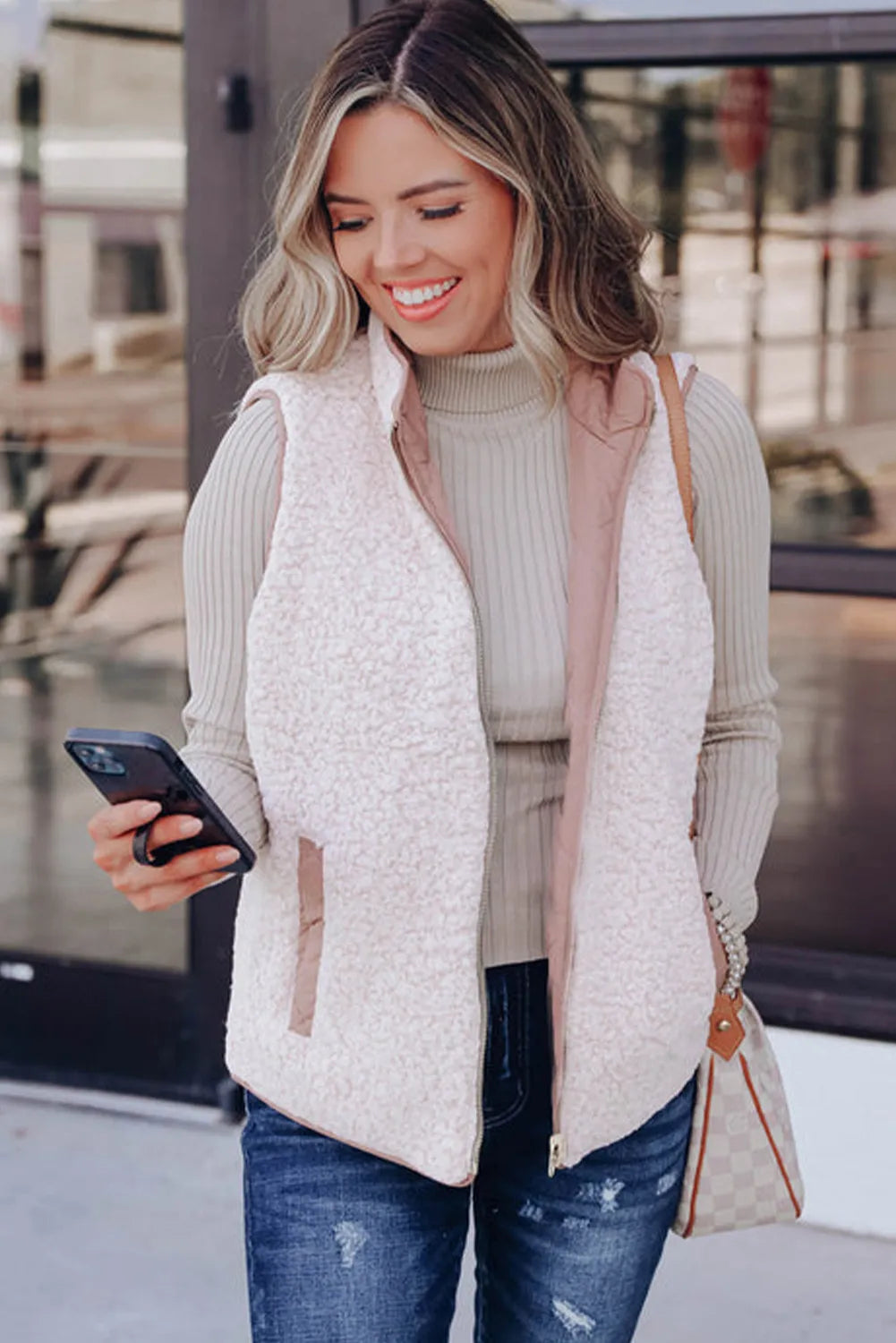 REVERSIBLE RETREAT VEST! Stylish woman wearing a pink Sherpa lined vest while checking her phone outdoors.