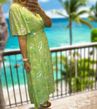 Model wearing a lime green Seashell Serenade midi dress with seashell print by Very J, set against a beach backdrop.