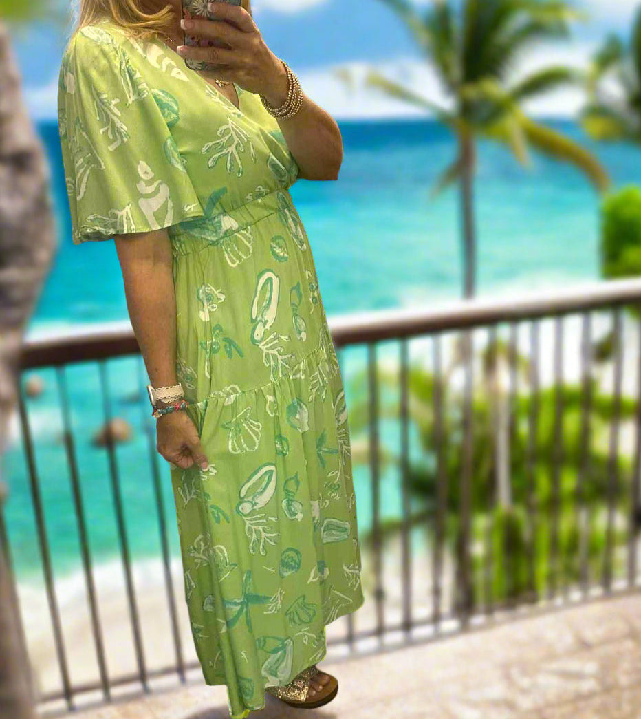 Model wearing a lime green Seashell Serenade midi dress with seashell print by Very J, set against a beach backdrop.