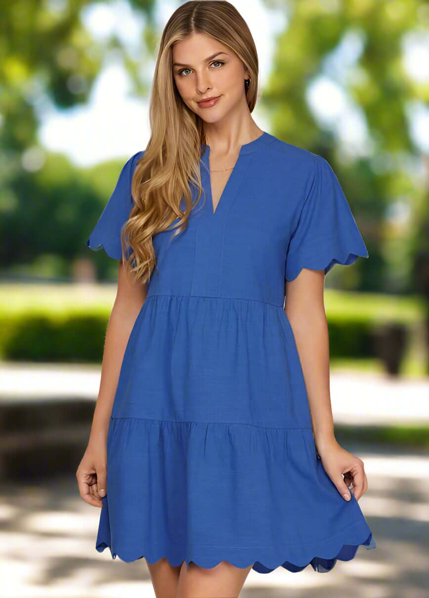 Woman in a cobalt blue tiered mini dress with scalloped sleeves and hem, showcasing modern elegance.