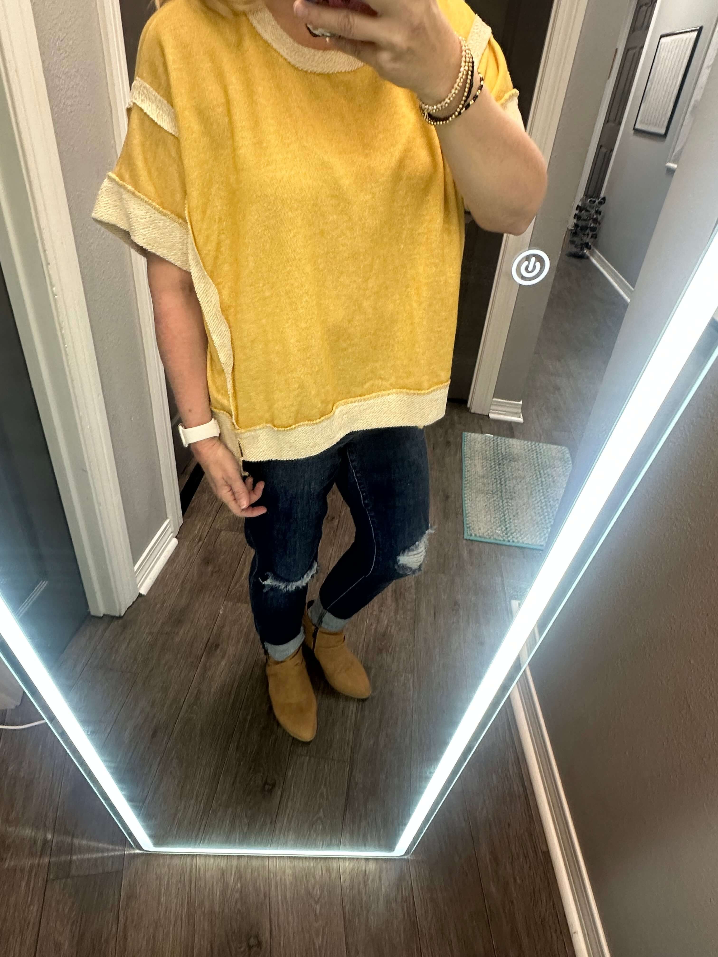 Model wearing casually cute mellow yellow top with distressed jeans in a mirror selfie, showcasing a relaxed style.