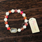 Pomina Level Up Bracelet in Ivory and Fiery Red featuring a rectangular glass gemstone with gold tone edge on a wooden surface.